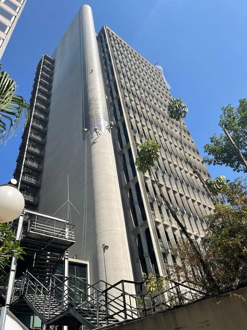 Profissional em corda limpando a fachada de concreto de um edifício
